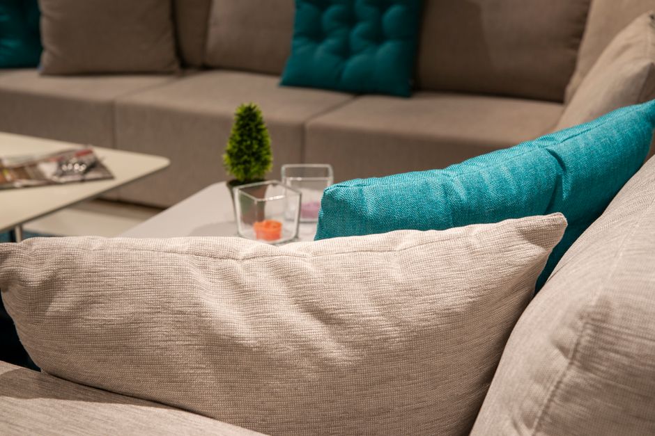 A white tufted fabric sofa with rolled arms and dark wooden legs situated in a bright, minimalist room with white paneled walls. The sofa appears clean and well-maintained, with no visible stains or dust. The hardwood floor beneath the sofa is polished, adding to the room's tidy appearance. The lighting emphasizes the softness of the upholstery and highlights the neatness of the space, reflecting professional cleaning and surface sanitisation by Carpet Cleaning Clapham, specialising in domestic surface cleaning and deep cleaning services.